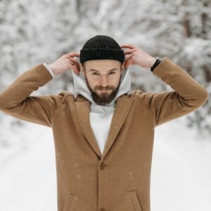 A man adjusting his beanie amidst a snowy winter forest.